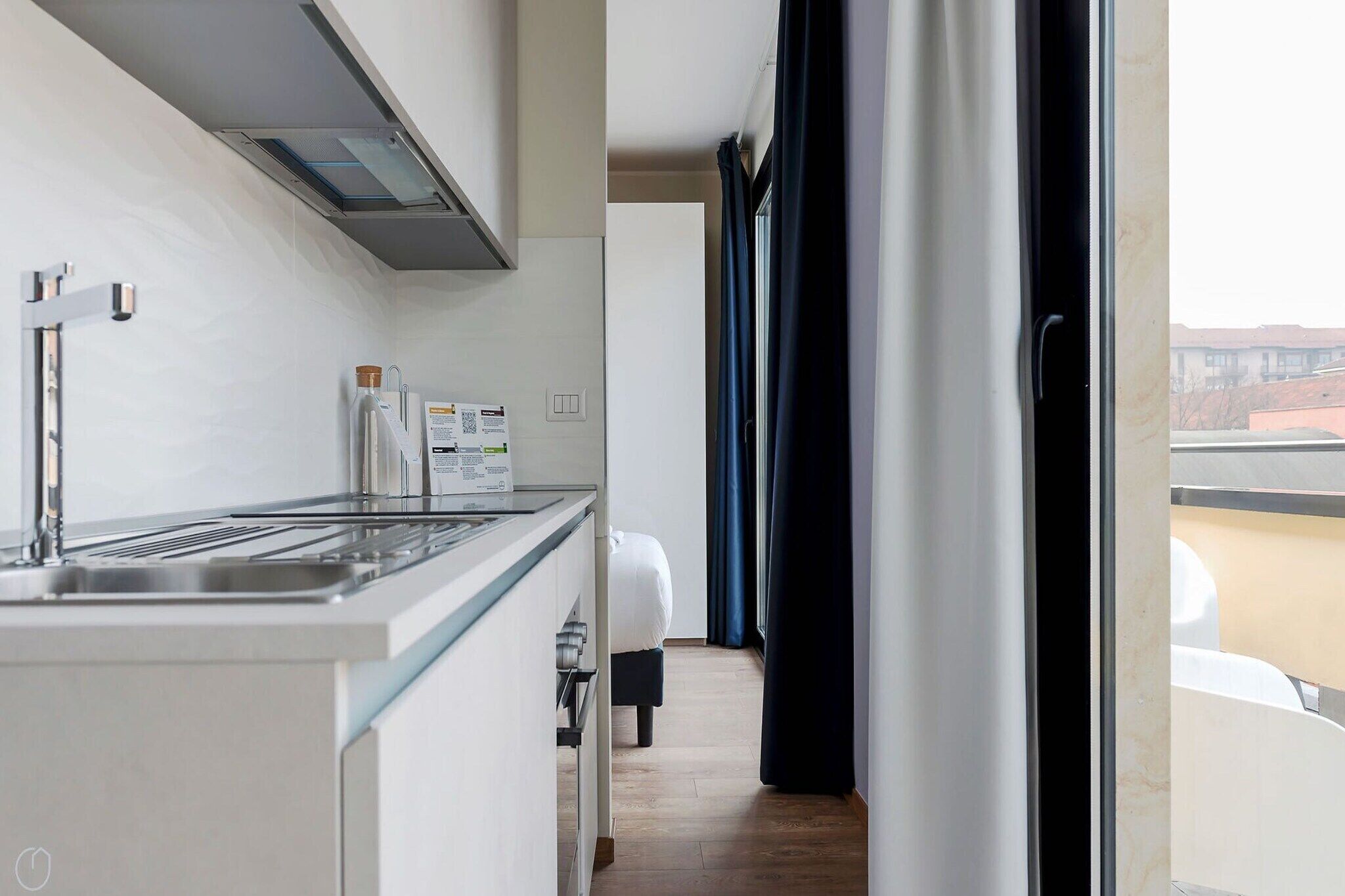 A modern kitchen with a built-in stove, a sink, and a countertop. There is a window with curtains, and a view of the outside.