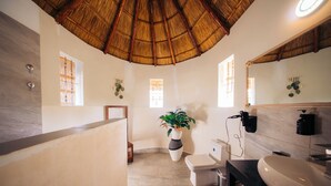 Ein Badezimmer mit Reetdach, einem großen Waschbecken, einer Toilette und einer Topfpflanze.