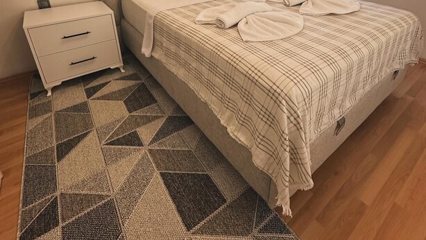 A bedroom with a bed, bedside tables, a patterned rug, and a window with blinds.