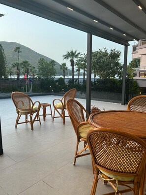 Un espace extérieur aménagé avec des meubles en osier, offrant une vue sur la mer et les montagnes.