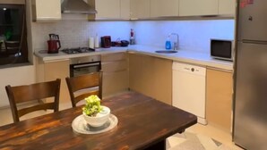 A modern kitchen with white cabinets, a stainless steel refrigerator, and a dining table with chairs.