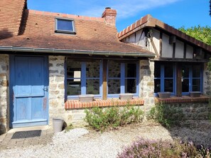 Ein Steinhaus mit einer blauen Tür, mehreren Fenstern und einem kleinen Garten.