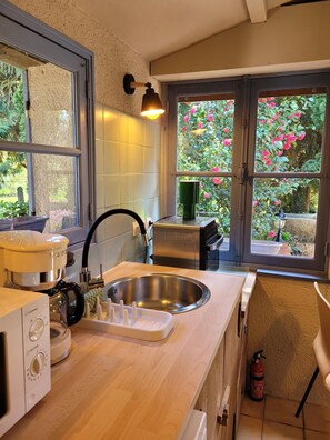 Eine Küche mit einer Spüle aus Edelstahl, einer Kaffeemaschine und einem Fenster mit Blick auf rosa Blumen.