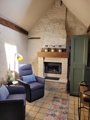 Ein gemütliches Wohnzimmer mit Kamin, blauem Sessel, kleinem Tisch mit Lampe und einem gemusterten Teppich.