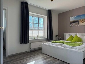 Quarto com cama, janela com cortinas, radiador e um quadro na parede.