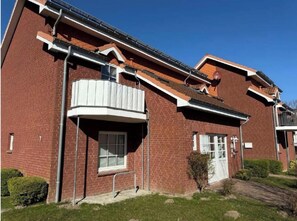 A red brick building with a white balcony, a door, and a small window. - Cozy Holiday Apartment ODIN in Schönhagen near the Beach (Brodersby-Schönhagen)