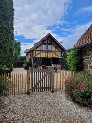 A traditional half-timbered house with a gravel driveway and a wooden gate. - Gîte Aire Holiday Home with Shared Pool, Communal Terrace, and Wi-Fi (Juvigny Val d'Andaine)