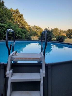 A swimming pool with a ladder leading into it, surrounded by greenery. - Gîte Aire Holiday Home with Shared Pool, Communal Terrace, and Wi-Fi (Juvigny Val d'Andaine)