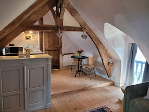 A cozy attic room with exposed wooden beams, a kitchen area with a microwave, and a dining table with chairs. - Gîte Aire Holiday Home with Shared Pool, Communal Terrace, and Wi-Fi (Juvigny Val d'Andaine)
