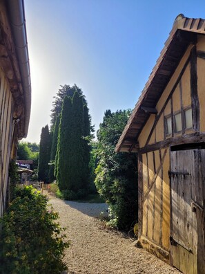 A narrow gravel path leading to a traditional building with exposed wooden beams and a sloped roof. - Gîte Aire Holiday Home with Shared Pool, Communal Terrace, and Wi-Fi (Juvigny Val d'Andaine)
