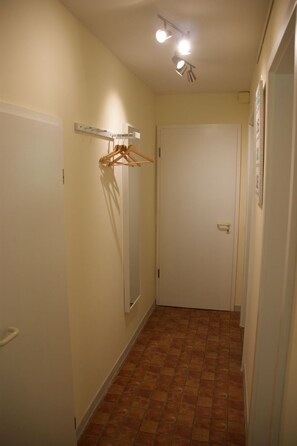 Ein schmaler Korridor mit Fliesenboden, einer weißen Tür und einem an der Wand befestigten Kleiderständer.