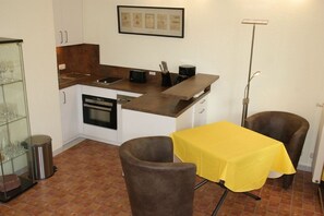 Una cucina compatta con zona pranzo, che include un tavolo con tovaglia gialla, due sedie e un cestino.