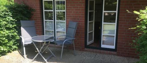 A patio with two chairs and a table, a brick wall, and a sliding glass door.