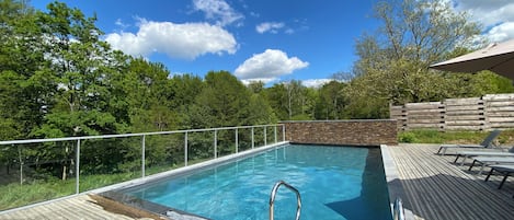 Ein rechteckiger Swimmingpool mit einer Metallleiter, umgeben von einer Holzterrasse und einer Steinmauer.
