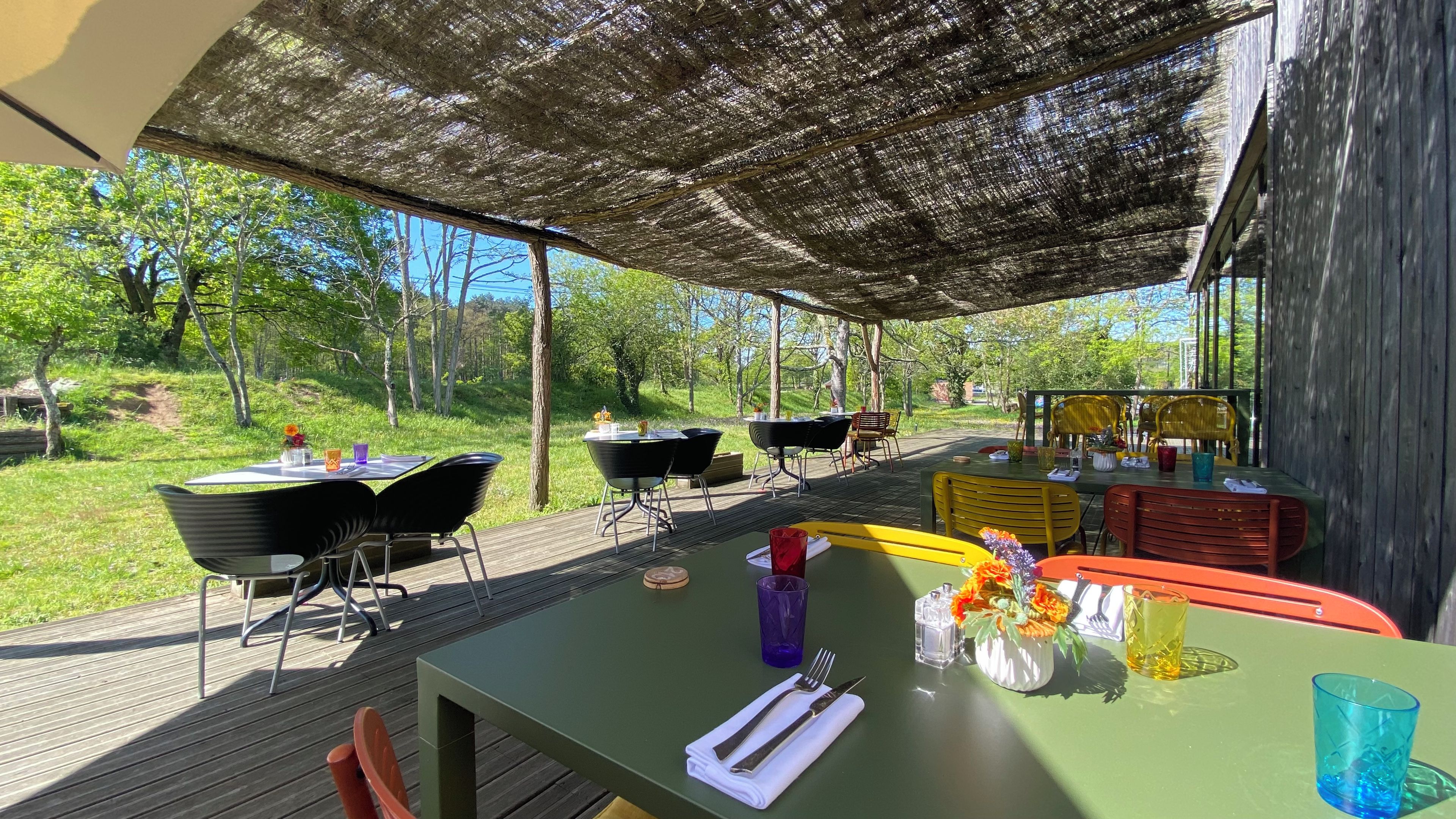Un área de comedor al aire libre con mesas y sillas, rodeada por una terraza de madera y un paisaje natural.