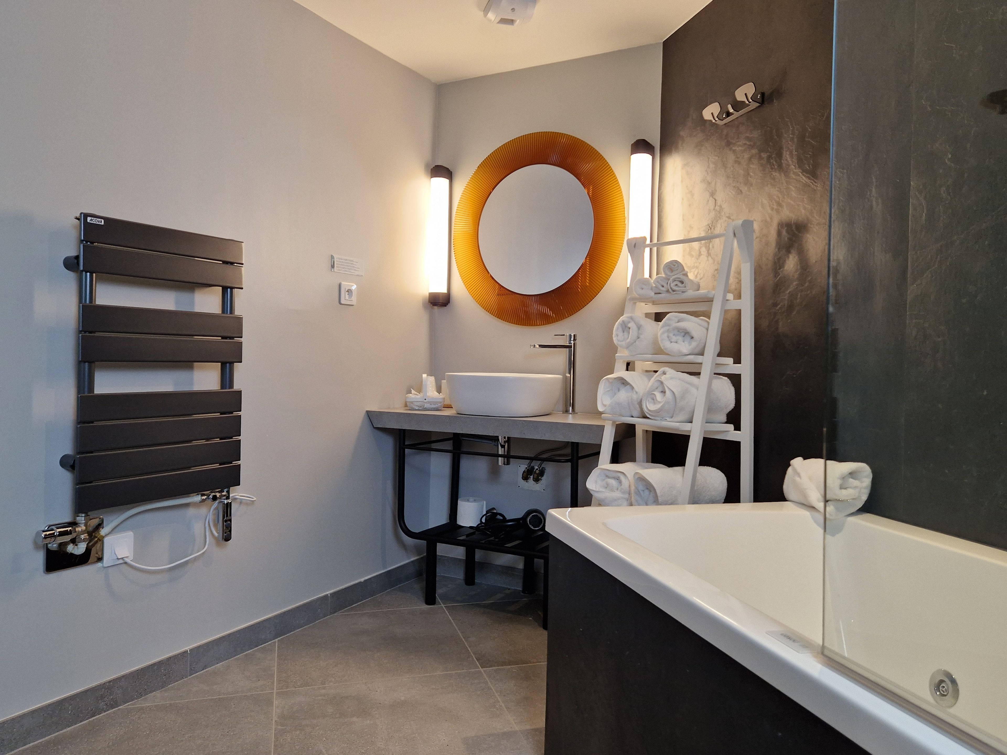 A modern bathroom with a towel rack, sink, mirror, and a heated towel rail.