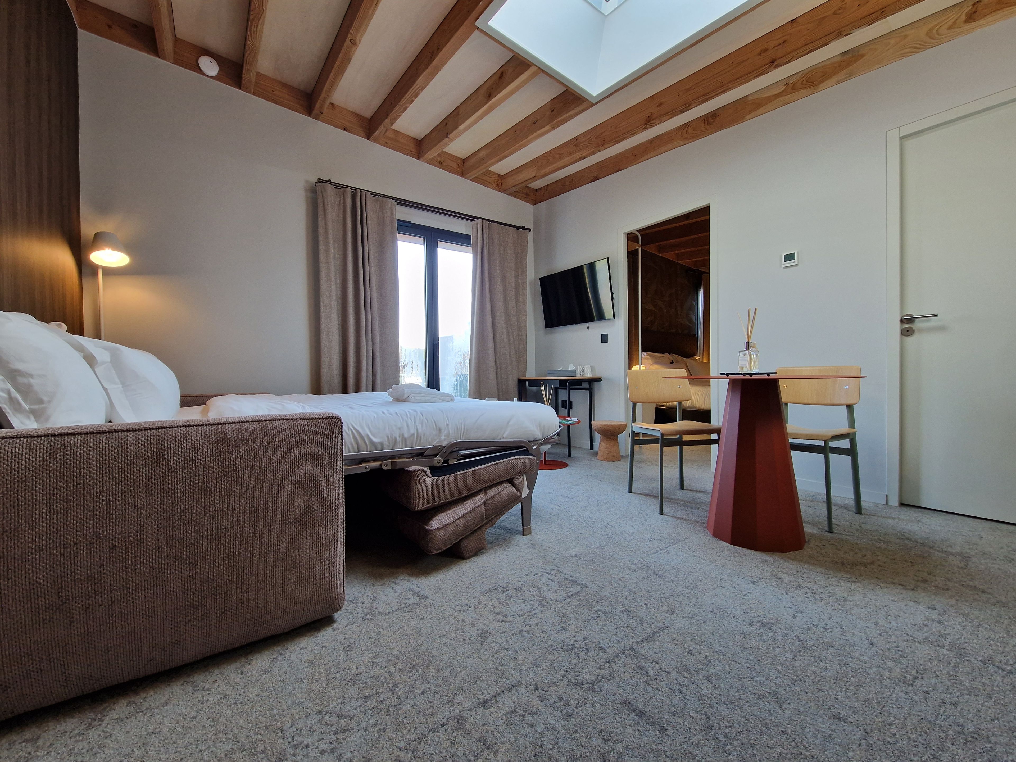 A hotel room with a bed, a sofa, a desk, a chair, a TV, and a door.
