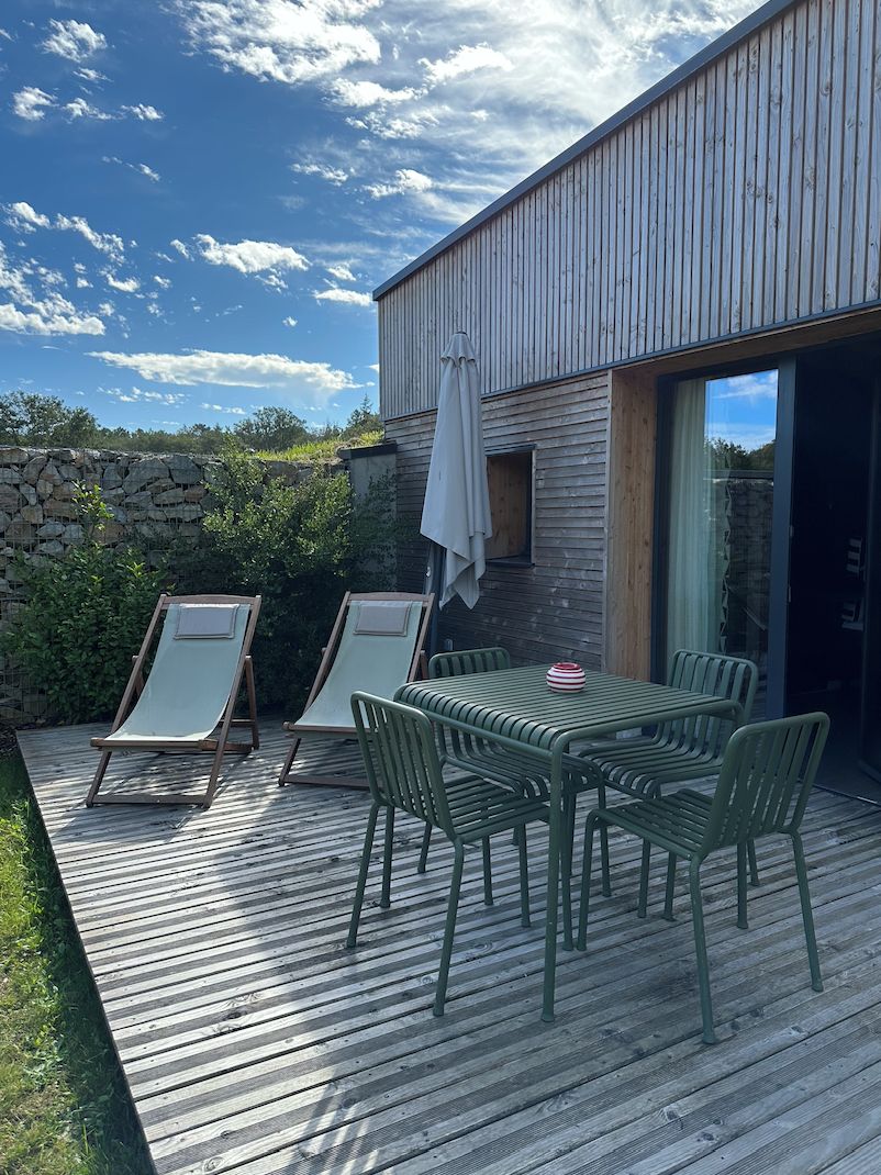 Une terrasse avec une table et des chaises, un mur en pierre et un bâtiment moderne doté de grandes fenêtres.