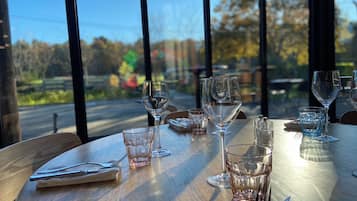 Una mesa de comedor con varias copas de vino y cubiertos, frente a una ventana con vistas a árboles y una carretera.