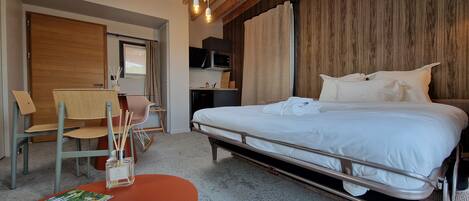 Une chambre d’hôtel comprenant un lit, un bureau avec une chaise, une armoire en bois, un four à micro-ondes et un plafond avec des poutres apparentes.