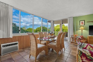 Ein Zimmer mit Esstisch und Stühlen, einem Fernseher und Blick auf Grünflächen.