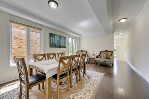 Un coin repas avec une table et des chaises en bois, un tapis et une vue sur un mur de briques à travers de grandes fenêtres.