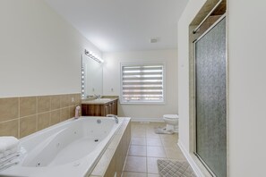 Een badkamer met een bad, douche, toilet en een raam met jaloezieën.