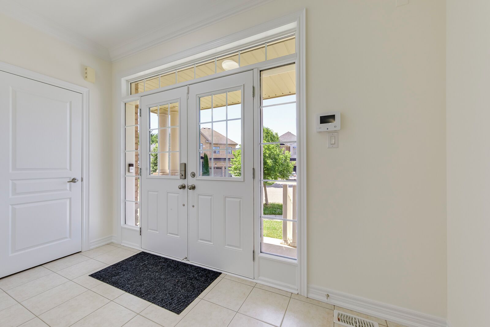 A clean, modern entryway with a double door, a small rug, and a thermostat on the wall.