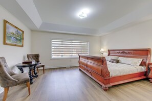 Een slaapkamer met een houten bed, een stoel, een klein tafeltje met schaakstukken en een schilderij aan de muur.