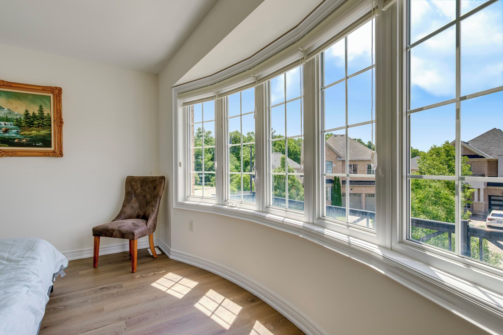 A room with a curved bay window, a chair, a bed, and a painting on the wall.