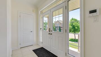 A hallway with a white door, a glass door with a view, and a thermostat on the wall.