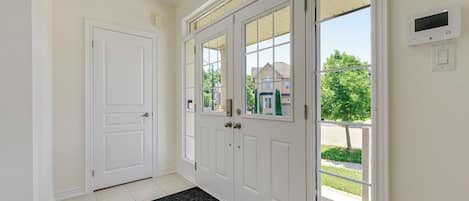 A hallway with a white door, a glass door with a view, and a thermostat on the wall.
