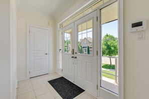 Un couloir avec une porte blanche, une porte vitrée donnant sur l’extérieur et un thermostat fixé au mur.