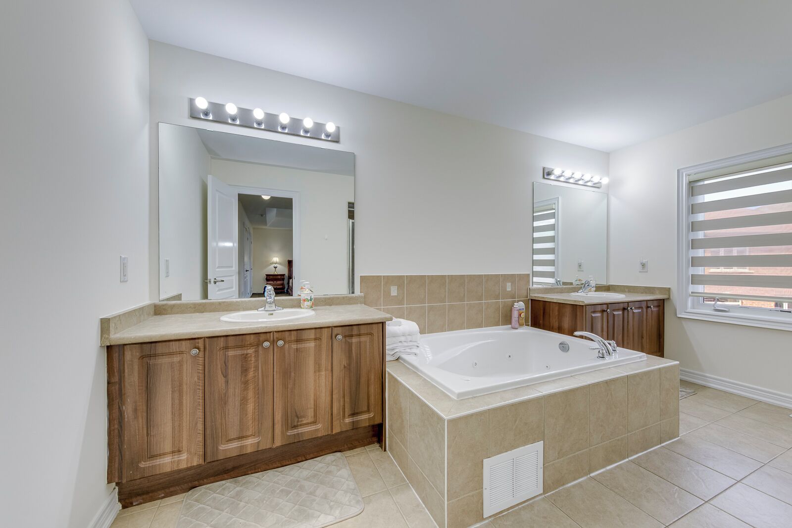 Une salle de bain moderne dotée d’un grand meuble-lavabo, d’une baignoire sur pieds et d’un grand miroir avec éclairage intégré.