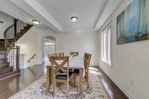 Een eetruimte met een tafel, stoelen, een trap en een schilderij aan de muur.
