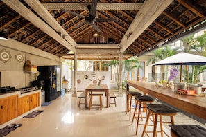 Una cocina amplia con armarios de madera, un refrigerador negro y una zona de comedor con mesa y sillas de madera.