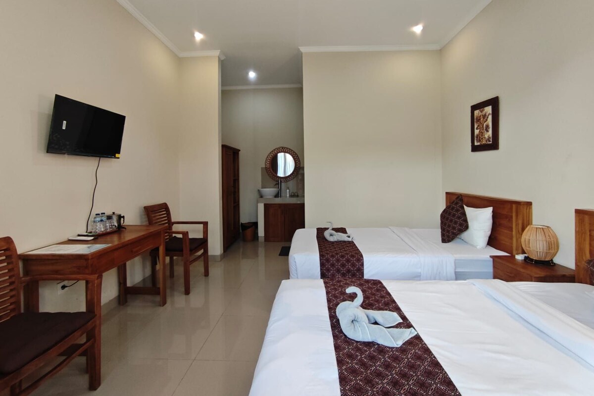 A hotel room with two beds, a desk, a television, and a bathroom visible in the background.