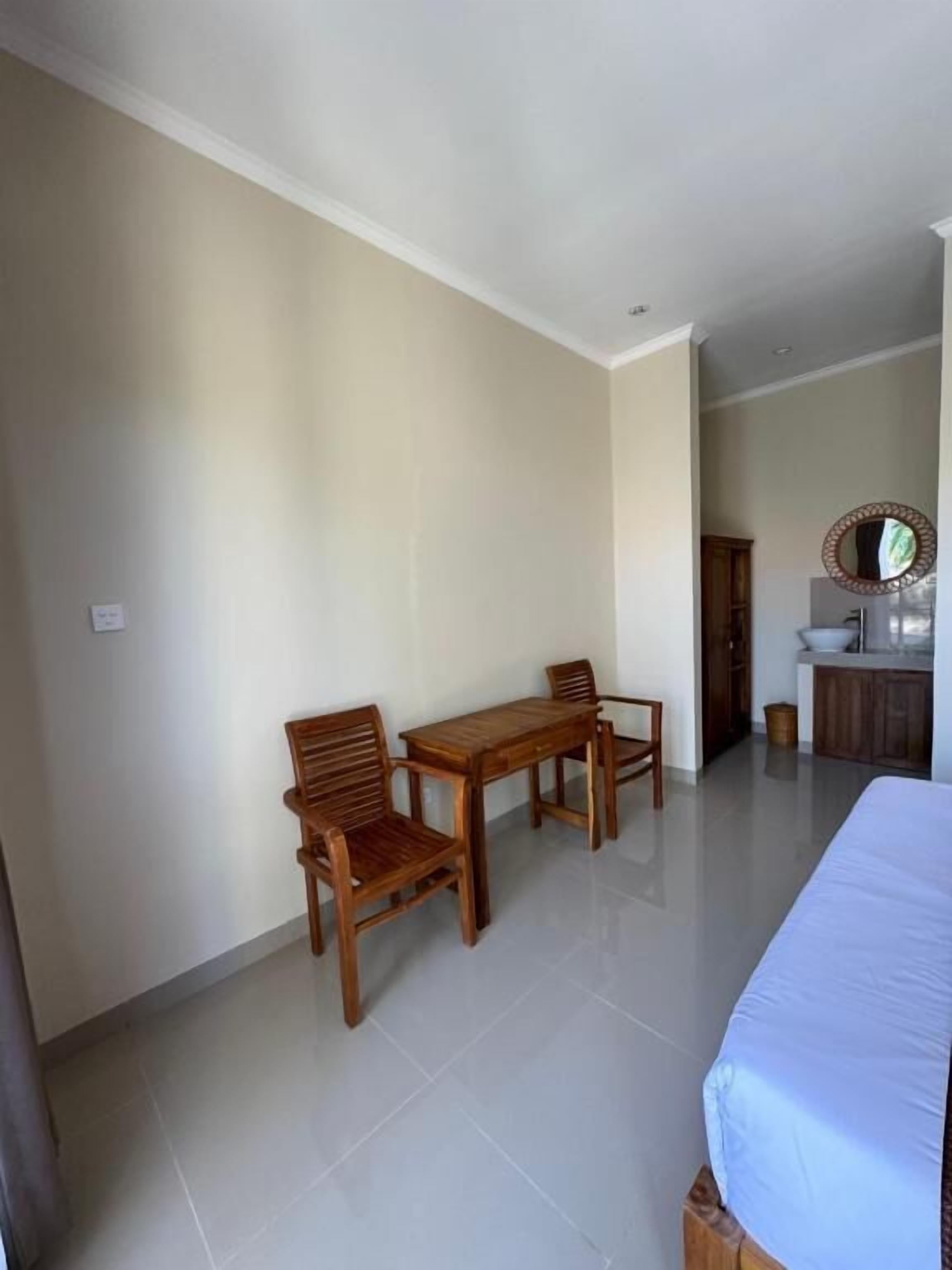 Habitación de hotel con cama, mesa, dos sillas, lavamanos y espejo.