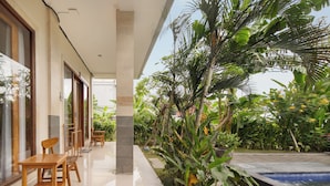 A modern outdoor area with a pool, wooden furniture, and lush tropical plants.