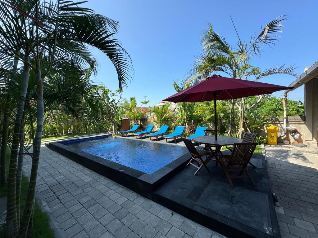 Una piscina con sillas de descanso y una mesa, rodeada de palmeras.