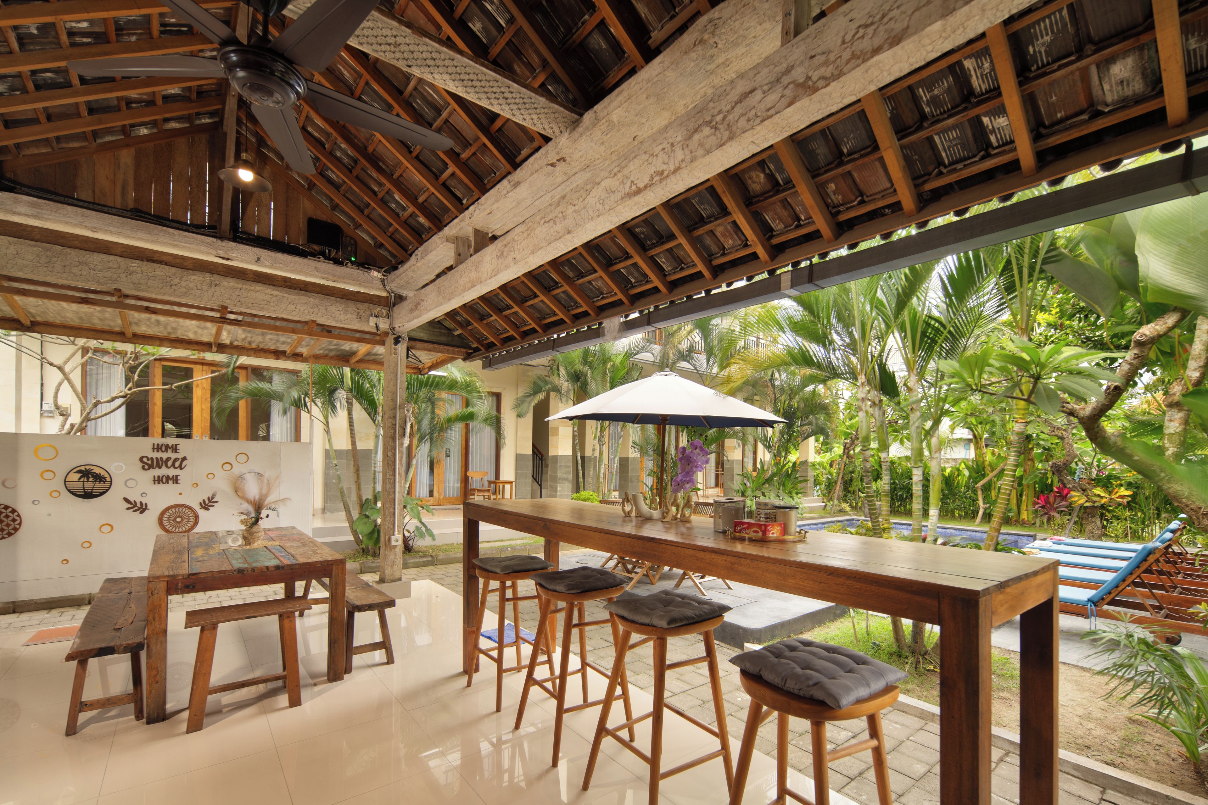 A spacious indoor area with a wooden ceiling, a bar area with stools, and a view of a pool with palm trees.