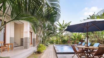 A poolside area with a table and chairs, surrounded by lush tropical plants.