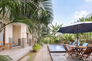 Zona junto a la piscina con mesa y sillas, rodeada de exuberante vegetación tropical.