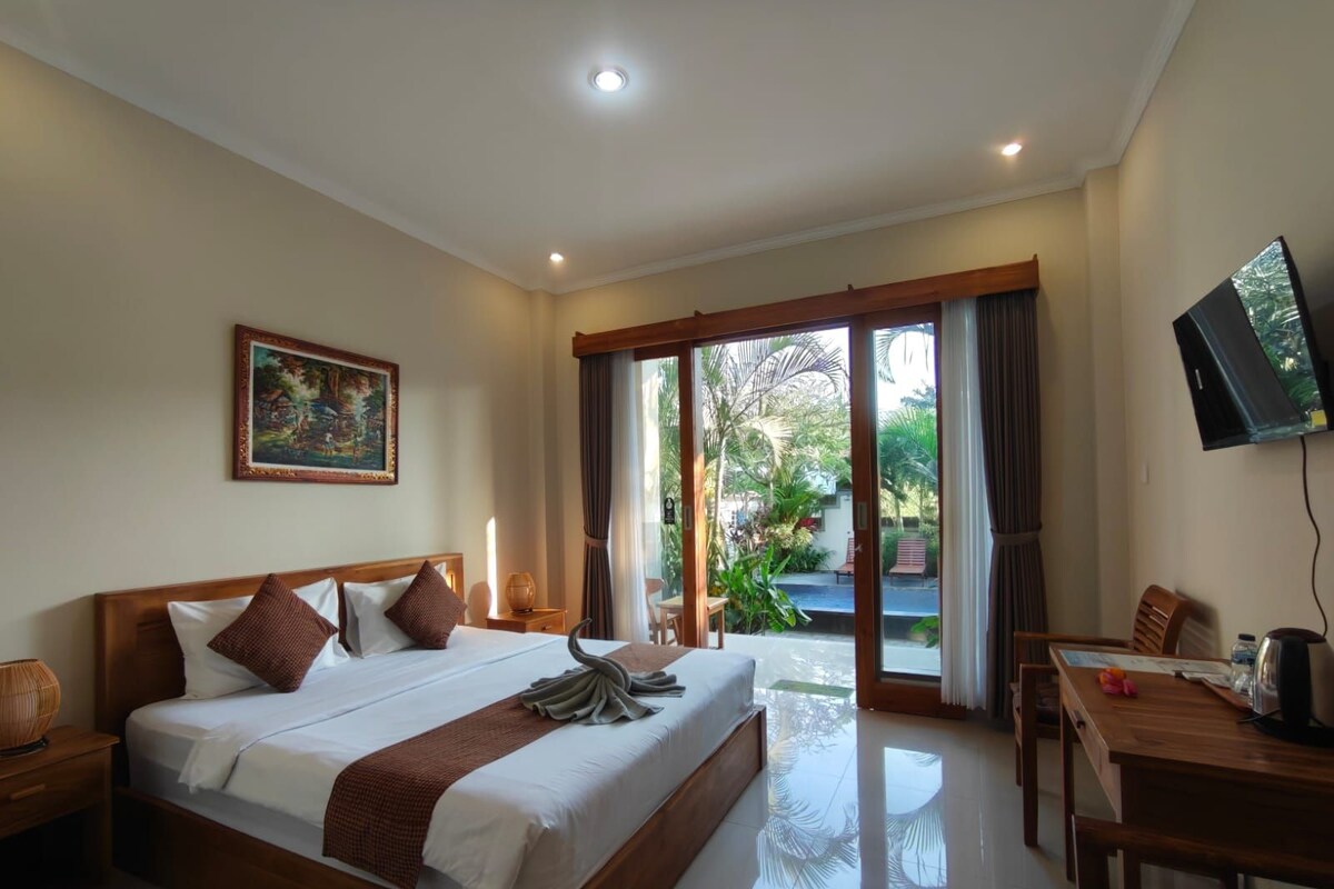 A hotel room with a large bed, a television, a dining table, and a view of the outdoors.