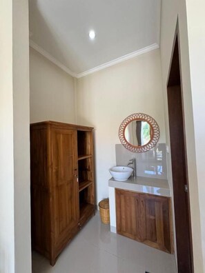A bathroom with a wooden cabinet, a white sink, and a mirror with a decorative frame. - Canggu Nadi 2  (Canggu)