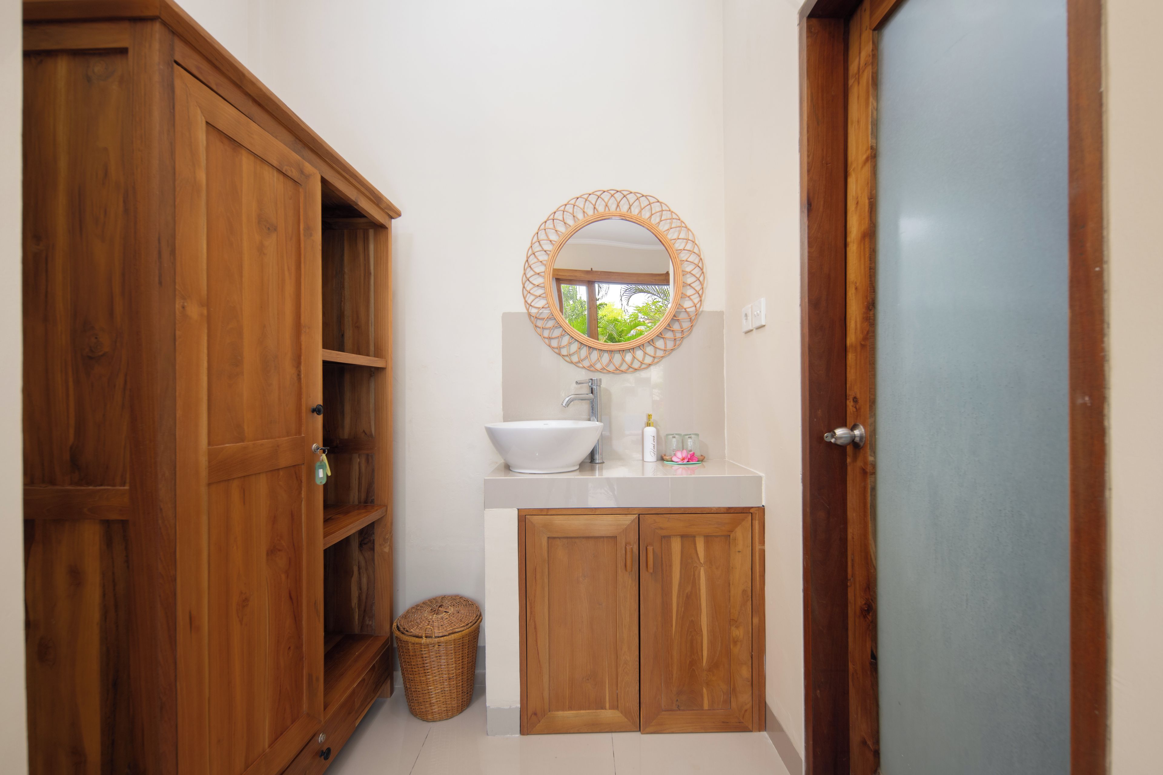 A bathroom with a wooden vanity, a white sink, a mirror with a woven frame, and a wicker basket.