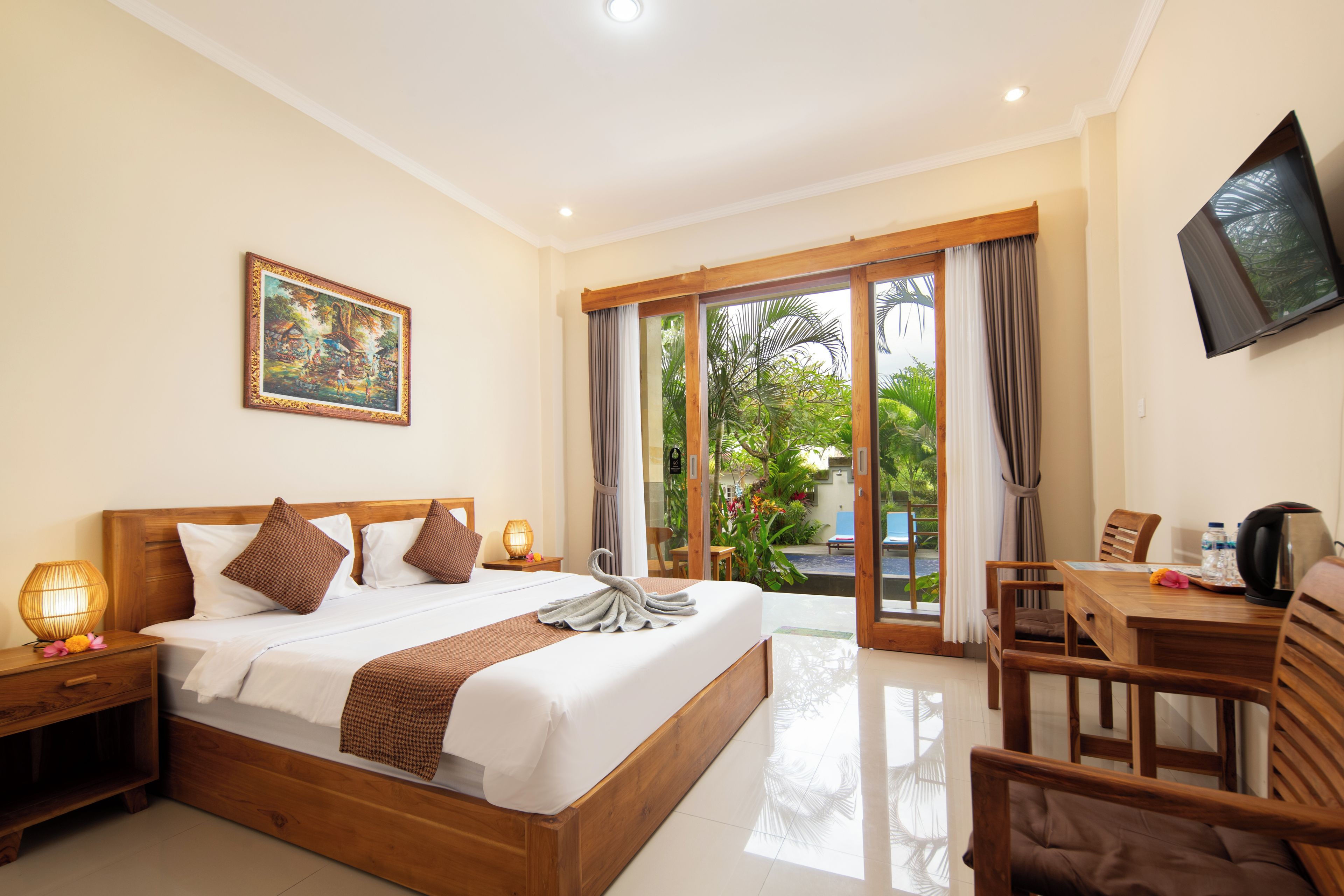 A hotel room with a large bed, a desk with a chair, a television, and a sliding glass door leading to a pool area.