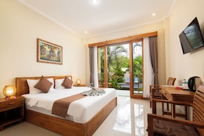 A hotel room with a large bed, a desk with a chair, a television, and a sliding glass door leading to a pool area. - Canggu Nadi 2  (Canggu)