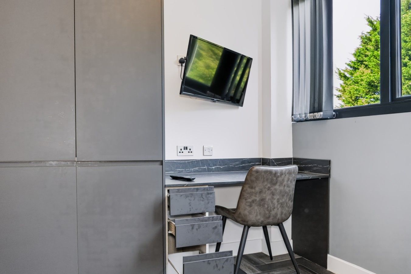 A modern kitchen with a built-in TV, grey cabinets, and a marble countertop.