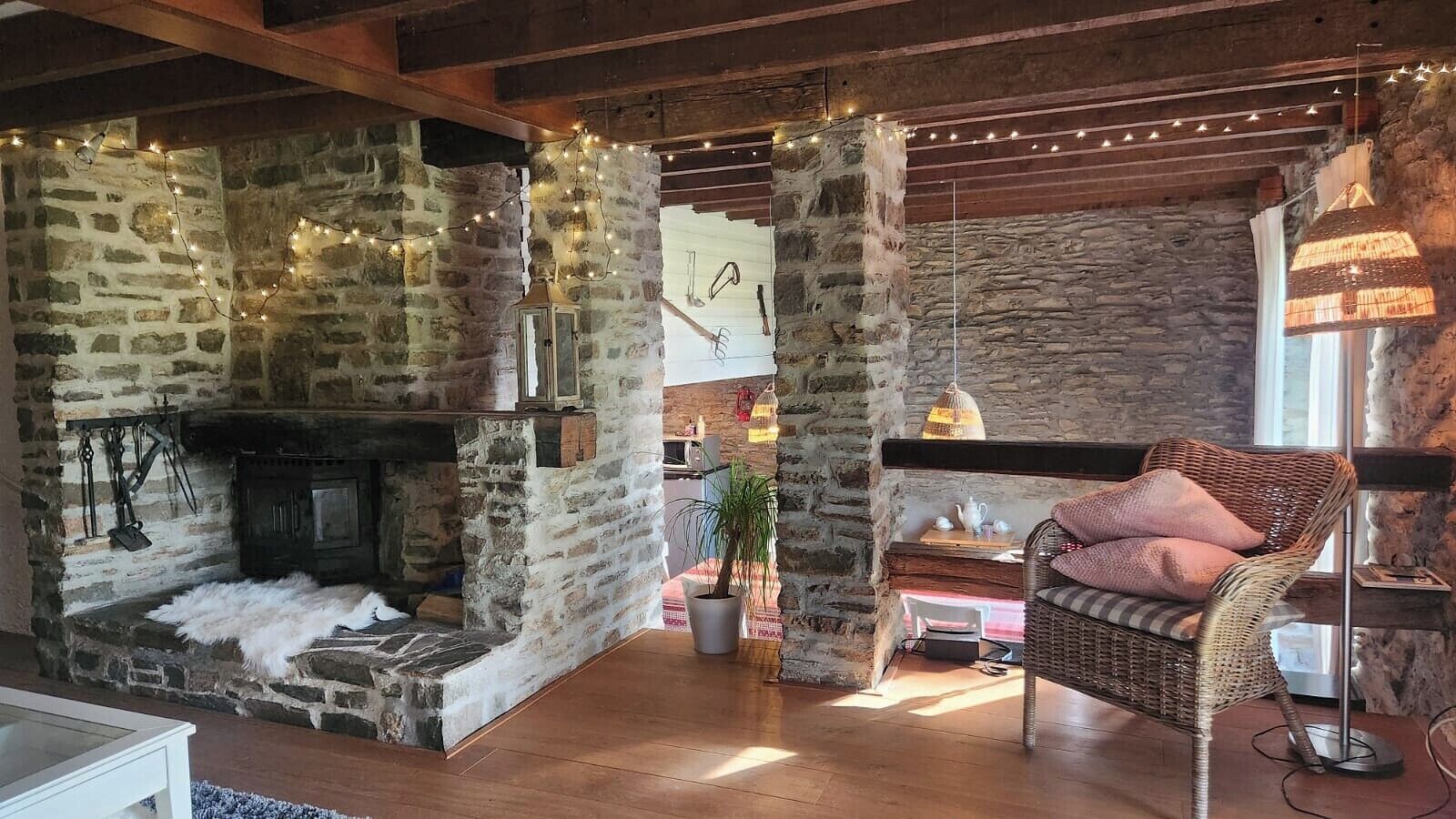 A rustic interior with exposed stone walls, a fireplace, a wicker chair, and string lights.